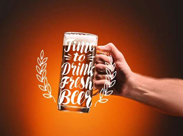 Обрезанный снимок человека, держащего кружку холодного пива на оранжевом фоне с вдохновением 