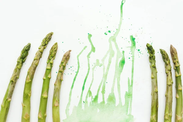 Draufsicht auf frische Spargelstangen auf weißer Oberfläche mit grünen Aquarellklecksen — Stockfoto