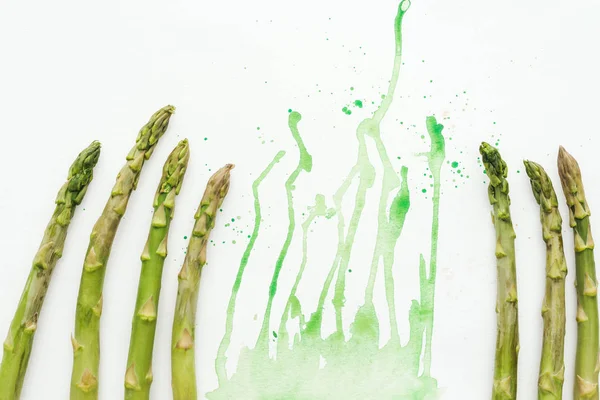 Vue de dessus des tiges d'asperges fraîches sur la surface blanche avec des taches d'aquarelle vertes — Photo de stock