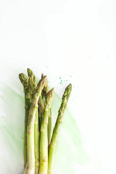 Vue de dessus du bouquet de tiges d'asperges sur la surface blanche avec des traits d'aquarelle verts — Photo de stock