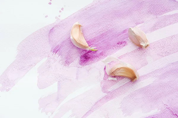Вид сверху на пряный сырой чеснок на белой поверхности с розовыми акварельными штрихами — стоковое фото
