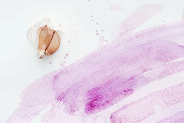 Top view of raw garlic on white surface with pink watercolor strokes and blots — Stock Photo