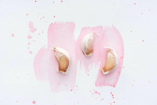 Top view of uncooked garlic on white surface with pink watercolor strokes — Stock Photo