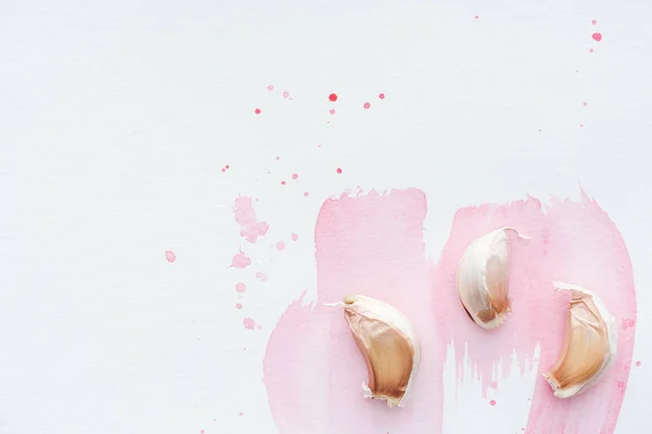 Вид сверху на пряный чеснок на белой поверхности с розовыми акварельными штрихами — стоковое фото