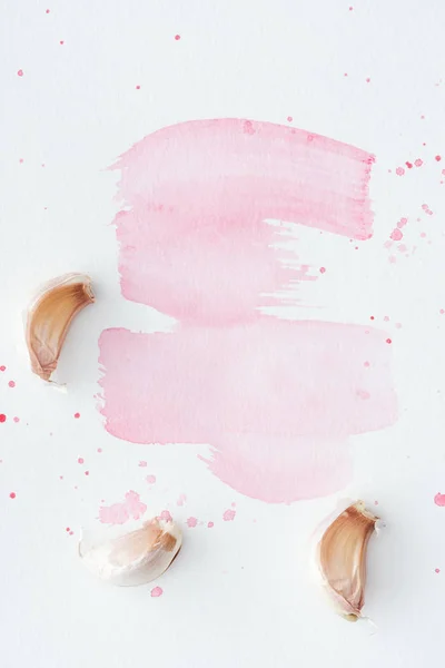 Vista superior de alho cru na superfície branca com traços de aquarela rosa — Fotografia de Stock