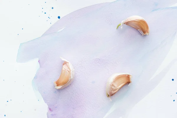 Draufsicht auf würzige Knoblauchstücke auf weißer Oberfläche mit violetten Aquarellstrichen — Stockfoto