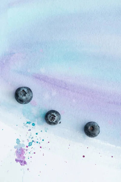 Vue de dessus des bleuets frais sur la surface blanche avec des traits d'aquarelle pourpre et des taches — Photo de stock