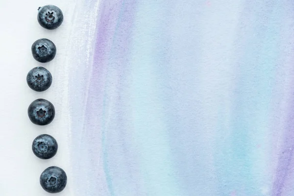 Draufsicht auf rohe köstliche Blaubeeren auf weißer Oberfläche mit violetten Aquarellstrichen — Stockfoto