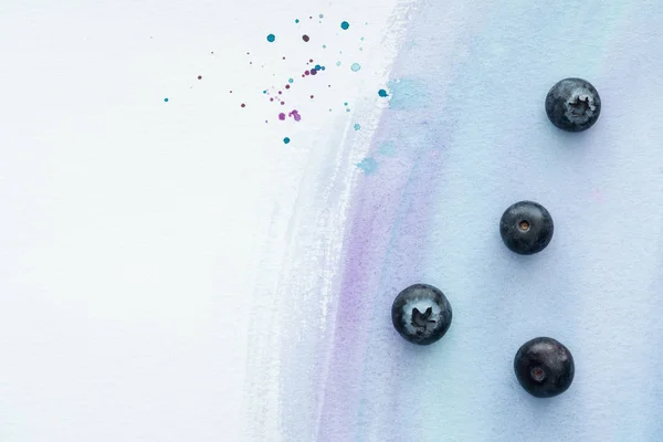 Top view of delicious ripe blueberries on white surface with purple watercolor strokes — Stock Photo