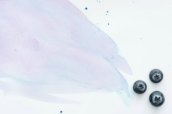 Top view of juicy blueberries on white surface with purple watercolor strokes — Stock Photo