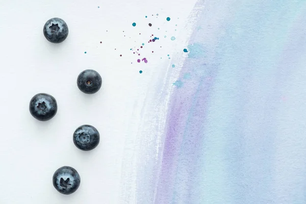 Vista dall'alto di deliziosi mirtilli sulla superficie bianca con tratti di acquerello viola — Foto stock