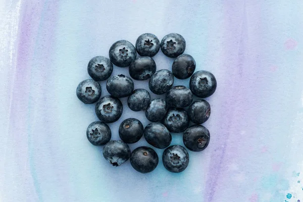 Draufsicht auf einen Haufen Blaubeeren auf weißer Oberfläche mit violetten Aquarellstrichen — Stockfoto