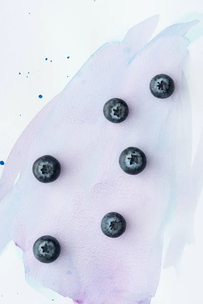 Vue de dessus des bleuets frais sur la surface blanche avec des traits d'aquarelle pourpre — Photo de stock