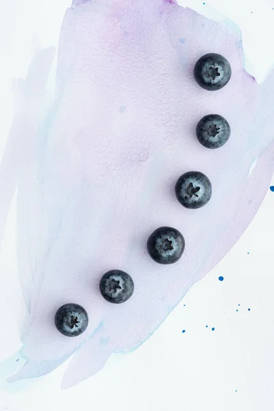 Top view of row of blueberries on white surface with purple watercolor strokes — Stock Photo