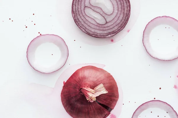 Draufsicht auf geschnittene würzige rote Zwiebel auf weißer Oberfläche mit rosa Aquarellfleck — Stockfoto