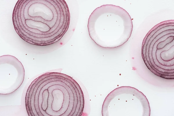 Top view of slices of spicy red onion on white surface with pink watercolor blots — Stock Photo