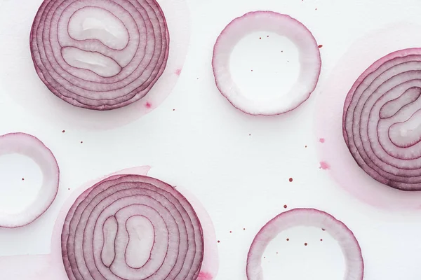 Draufsicht auf würzige rote Zwiebelscheiben auf weißer Oberfläche mit rosa Aquarellflecken — Stockfoto