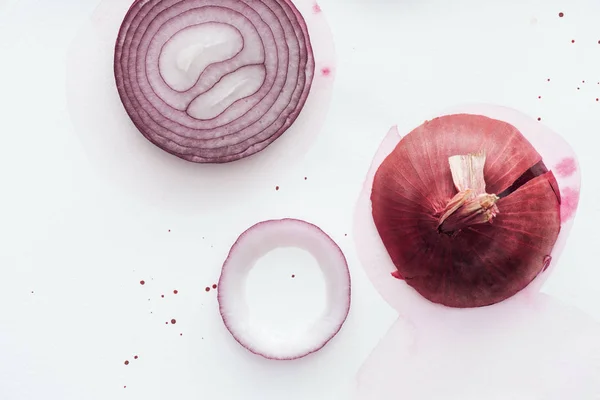 Top view of raw whole red onion with slice on white surface with pink watercolor blots — Stock Photo