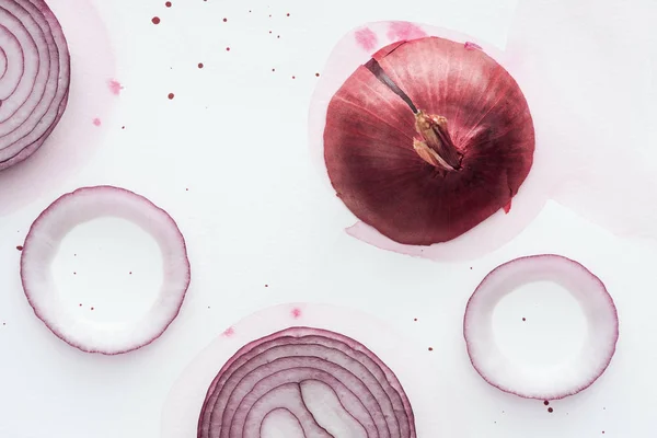 Draufsicht auf rohe ganze rote Zwiebel mit Ringen auf weißer Oberfläche mit rosa Aquarellflecken — Stockfoto