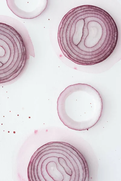 Draufsicht auf rohe Scheiben roter Zwiebel auf weißer Oberfläche mit rosa Aquarellflecken — Stockfoto