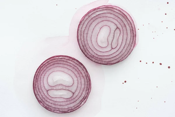 Vue de dessus de deux tranches d'oignon rouge sur la surface blanche avec taches d'aquarelle rose — Photo de stock