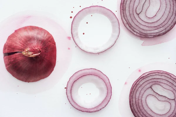 Vista superior de cebola vermelha com fatias e anéis na superfície branca com manchas de aquarela rosa — Fotografia de Stock