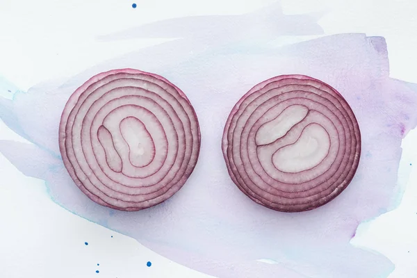 Draufsicht auf zwei Scheiben roter Zwiebel auf weißer Oberfläche mit violetten Aquarellstrichen — Stockfoto