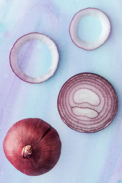 Top view of raw sliced red onion on white surface with blue watercolor strokes — Stock Photo