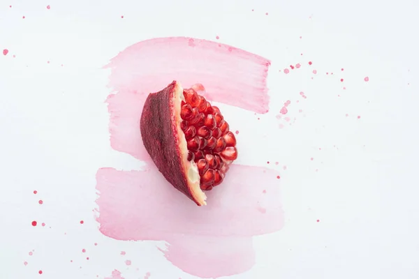 Top view of piece of pomegranate on white surface with pink watercolor strokes — Stock Photo