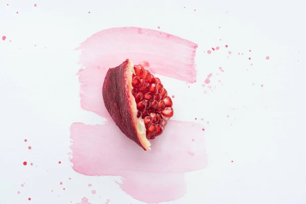 Vista dall'alto di un pezzo di melograno sulla superficie bianca con tratti di acquerello rosa — Foto stock