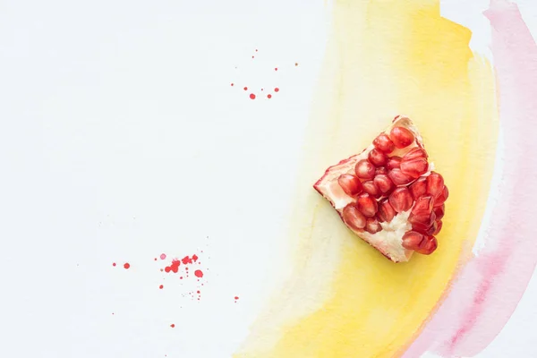 Vue de dessus de délicieux morceau de grenade sur la surface blanche avec des traits d'aquarelle jaune et rose — Photo de stock