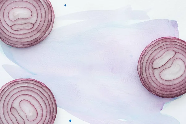 Top view of sliced red onion on white surface with purple watercolor strokes — Stock Photo