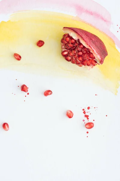 Ansicht von reifem Granatapfel auf weißer Oberfläche mit gelben und rosa Aquarellstrichen — Stockfoto