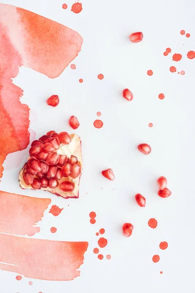 Top view of ripe pomegranate on white surface with red watercolor strokes — Stock Photo