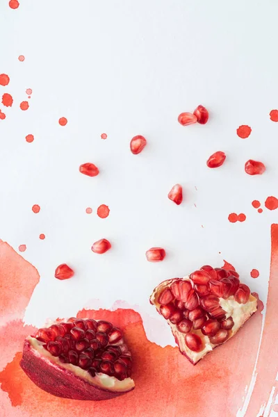 Top view of delicious pomegranate on white surface with red watercolor strokes — Stock Photo