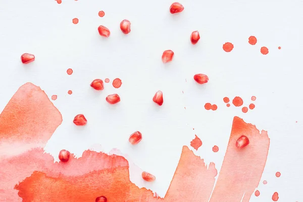 Top view of pomegranate seeds on white surface with red watercolor strokes — Stock Photo