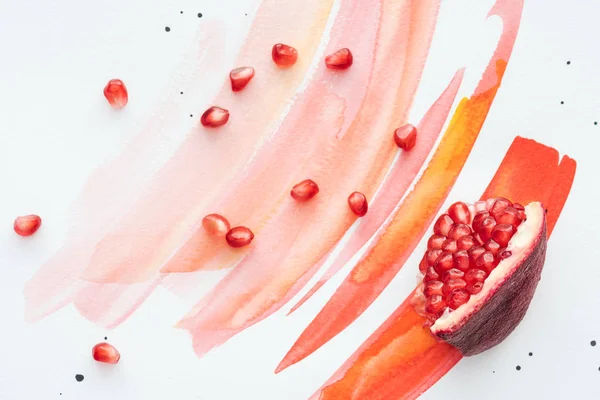 Draufsicht auf Granatapfelstück mit Kernen auf weißer Oberfläche mit roten Aquarellstrichen — Stockfoto