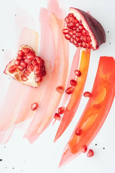 Top view of pieces of pomegranate on white surface with red watercolor strokes — Stock Photo