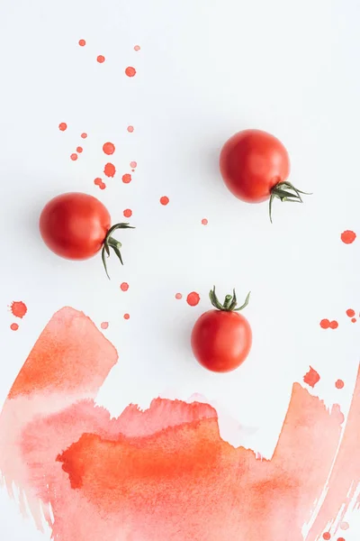 Draufsicht auf reife Kirschtomaten auf weißer Oberfläche mit roten Aquarellstrichen und Flecken — Stockfoto