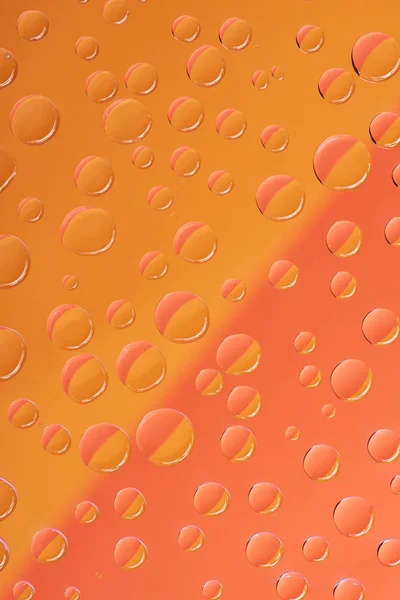 Nahaufnahme transparenter Wassertropfen auf leuchtend rotem und orangefarbenem Hintergrund — Stockfoto