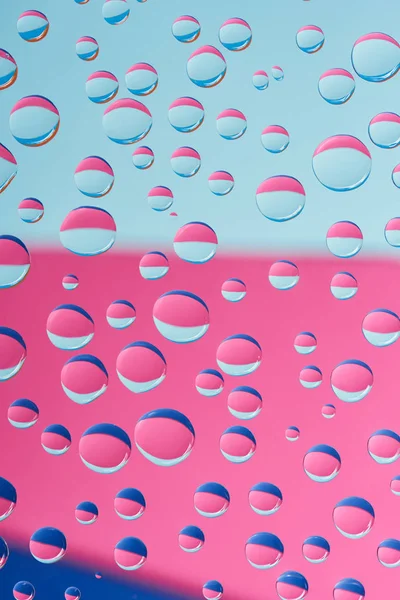 Vue rapprochée de gouttelettes transparentes sur fond abstrait rose et bleu — Photo de stock