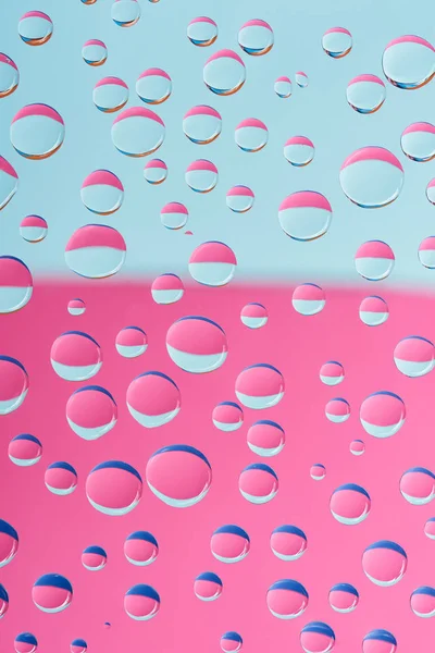 Vista de cerca de gotas de agua transparentes sobre fondo abstracto rosa y azul - foto de stock