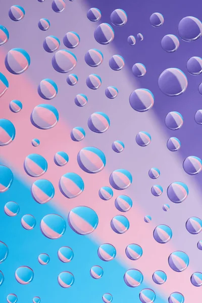 Vista de cerca de gotas de agua transparentes sobre fondo de colores brillantes - foto de stock