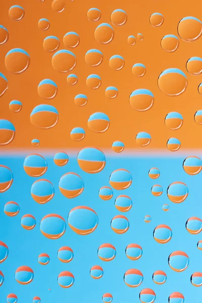 Vista de cerca de gotas de agua transparentes sobre fondo azul y naranja - foto de stock