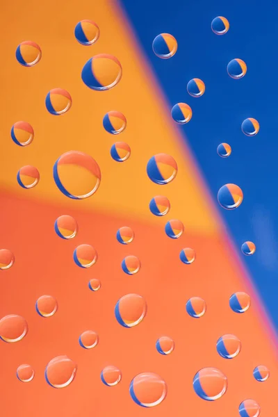 Vista de cerca de gotas de agua transparentes sobre un fondo colorido - foto de stock