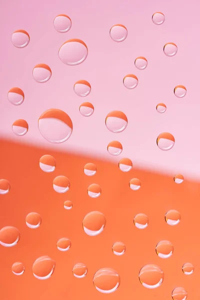 Vista de cerca de gotas de agua tranquilas transparentes sobre fondo rosa y naranja - foto de stock