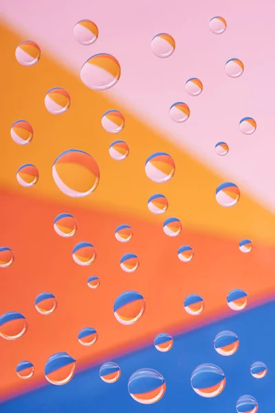 Vista de cerca de gotas de agua tranquilas transparentes sobre un fondo colorido - foto de stock