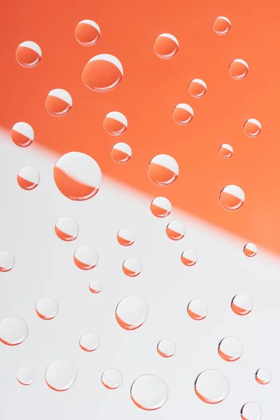 Vista de cerca de gotas de agua tranquilas transparentes sobre fondo blanco y naranja - foto de stock