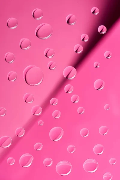 Vista de cerca de gotas transparentes de rocío limpio sobre fondo rosa - foto de stock