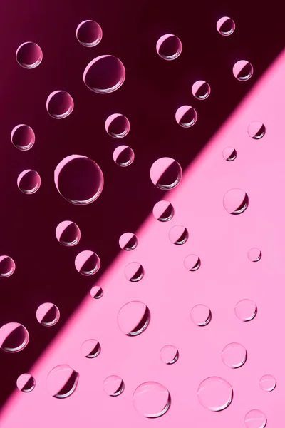 Vista de cerca de gotas de rocío transparente sobre fondo rosa - foto de stock